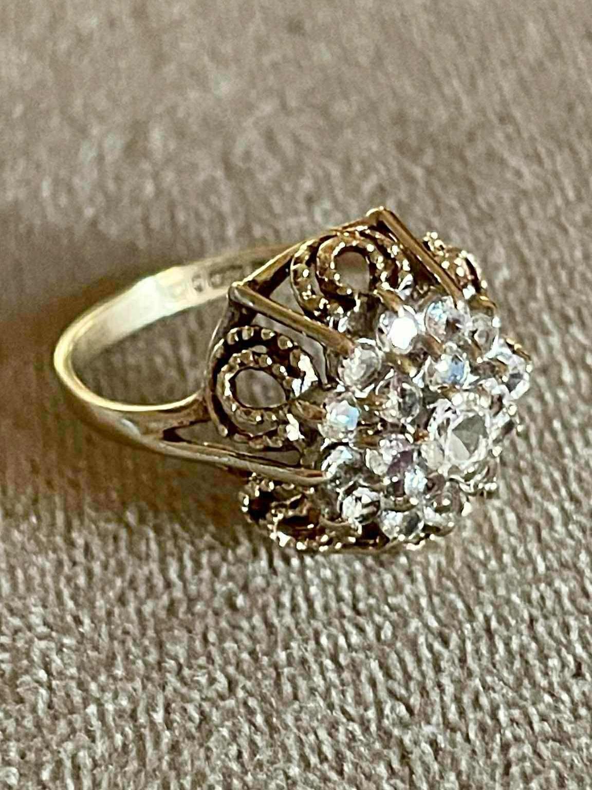 Bague vintage en argent ornée de pierres brillantes, au design délicat et travaillé, sur un fond texturé.