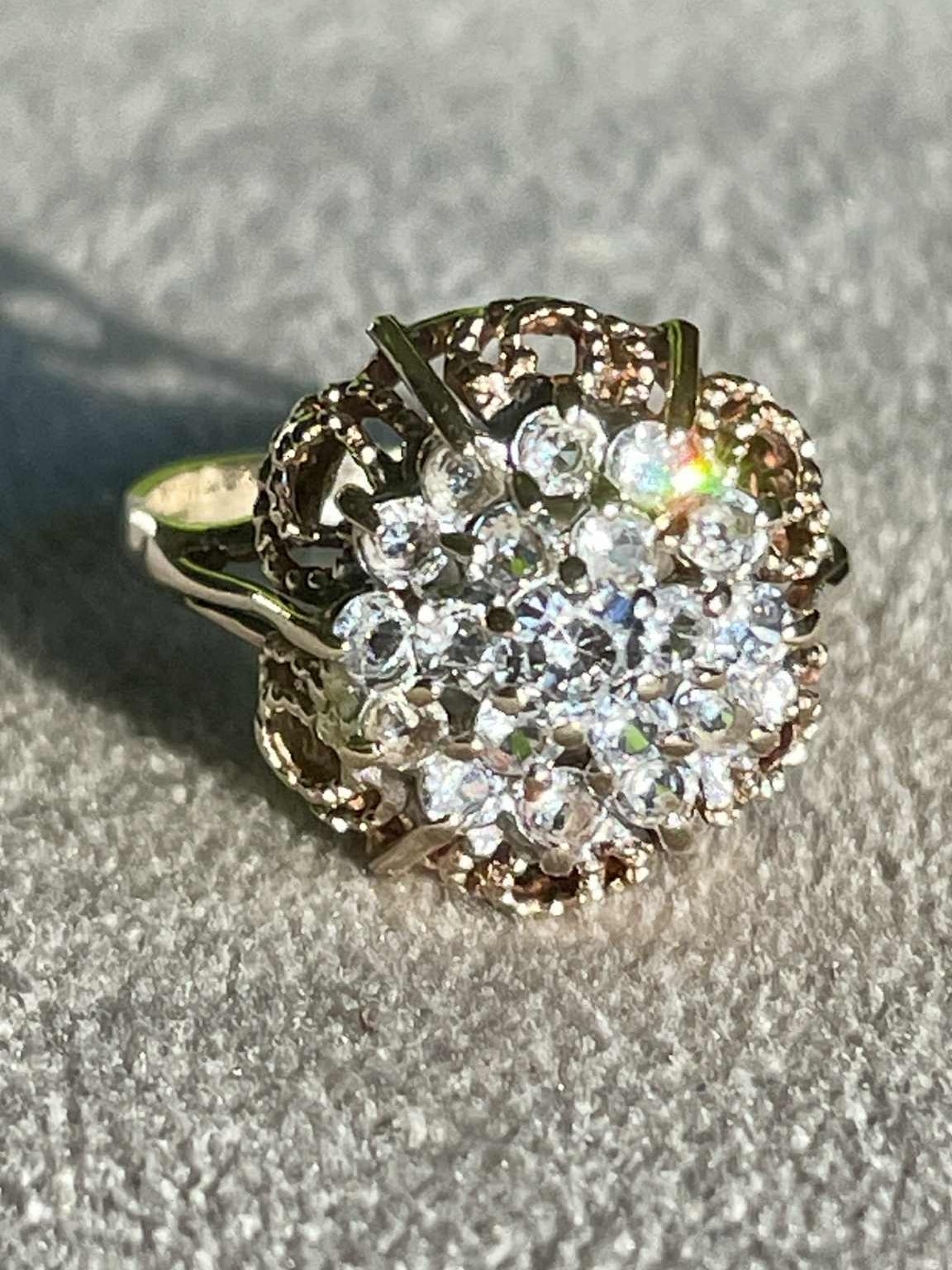 Bague vintage en or et pierres précieuses, avec un design rond et étincelant sur un fond clair.