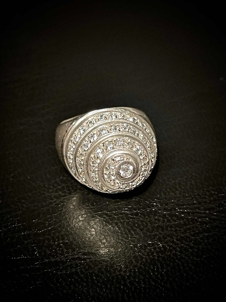 Bague dôme en argent massif de style vintage, ornée d'un pavage de pierres étincelantes disposées en spirale concentrique. Le bijou est photographié de face sur un support en cuir noir texturé