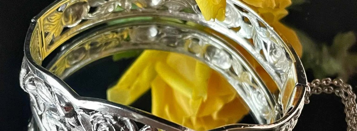 Bracelet jonc en argent ciselé avec un décor de roses en relief, posé sur un miroir à côté d'une rose jaune