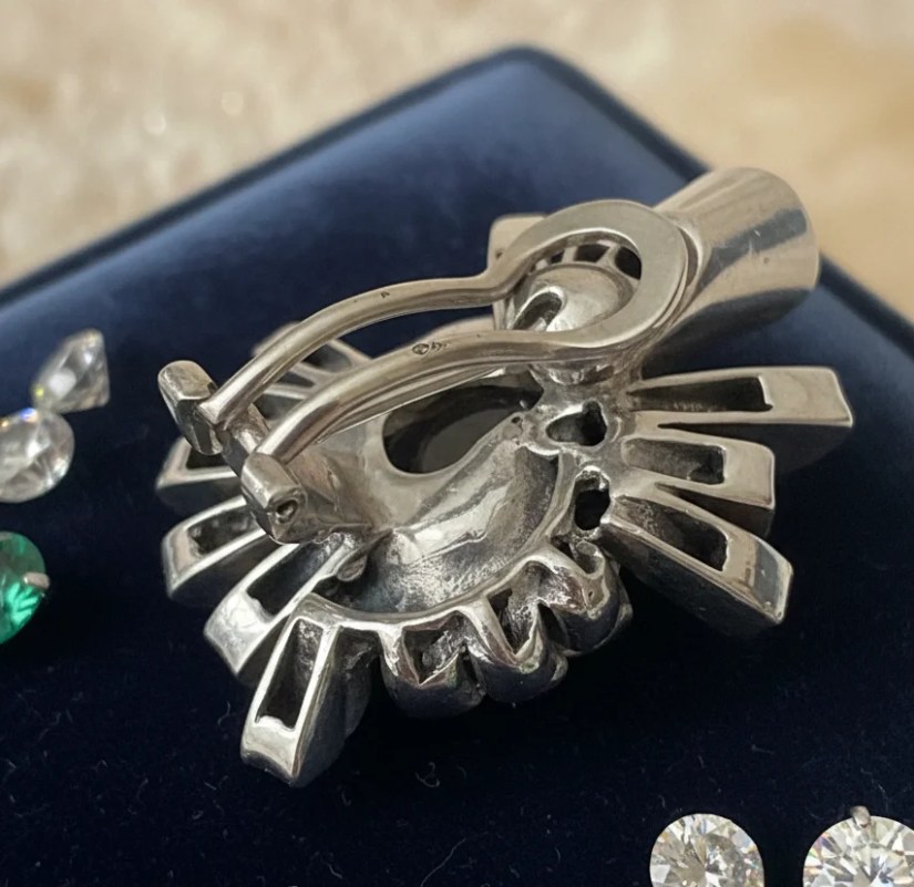 Vue détaillée du revers d'une boucle d'oreille ancienne en argent montrant le poinçon d'orfèvre et le système de fermeture à clip oméga. Le bijou présente une structure complexe aux lignes géométriques, posé sur un écrin en velours bleu.